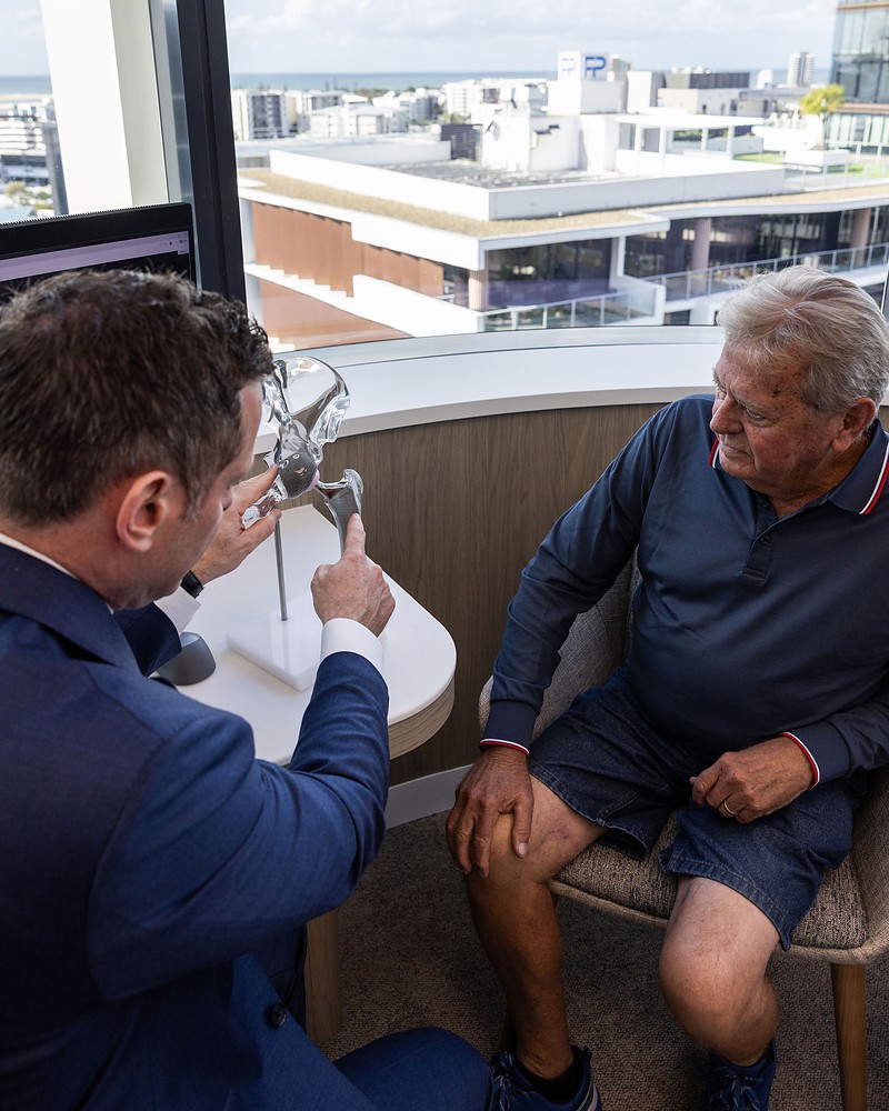 Professor Daevyd Rodda showing a hip replacement implant to a patient in the consulting room